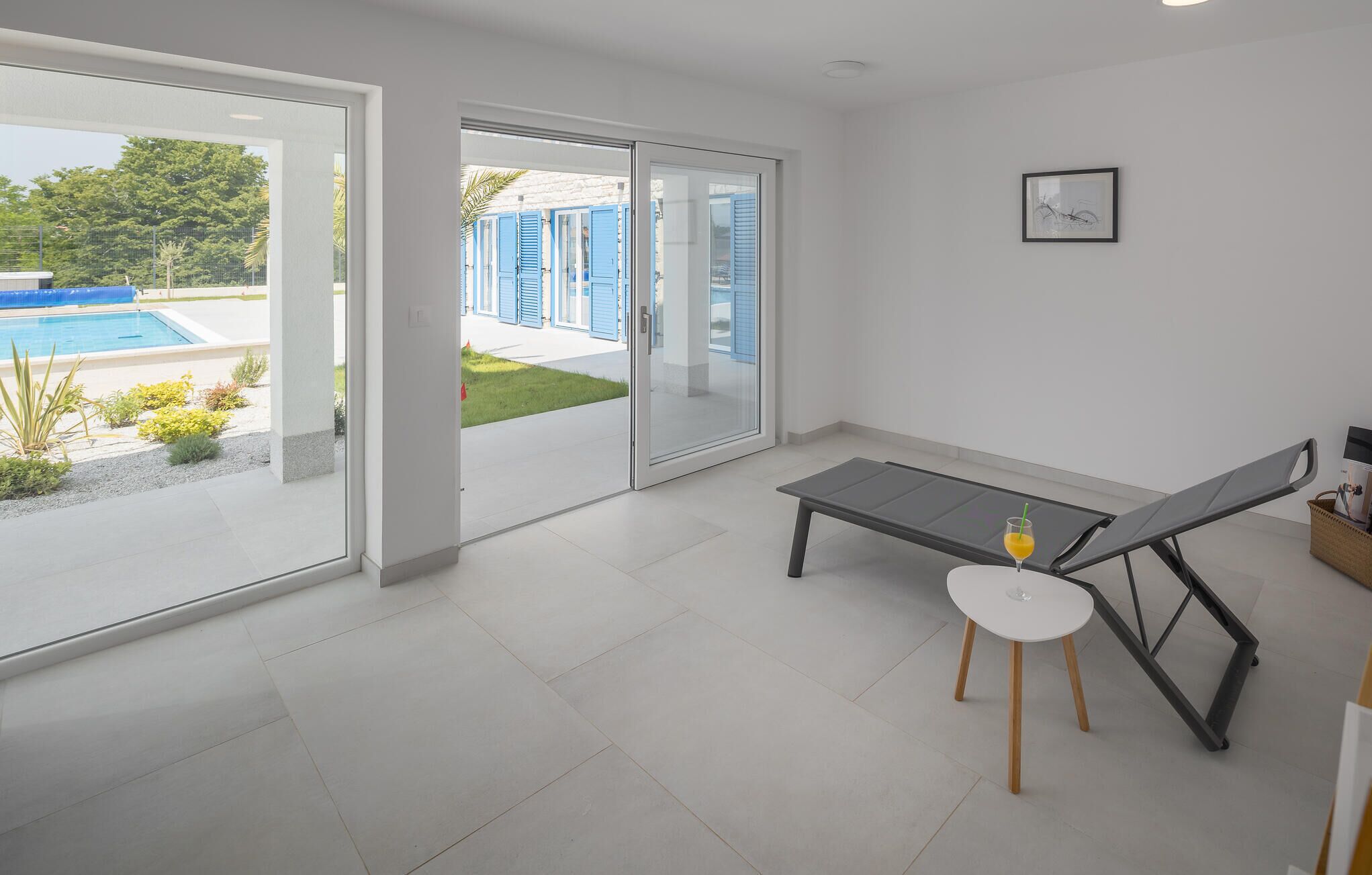 Quarto moderno com porta de vidro que dá para uma área de piscina, uma pequena mesa com uma cadeira e um quadro na parede.