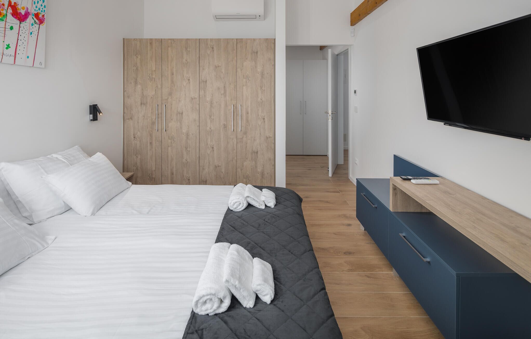 A hotel room with a bed, a wooden wardrobe, a TV, and a desk.
