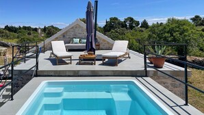 A rooftop pool area with two lounge chairs, a table, and a large pool.