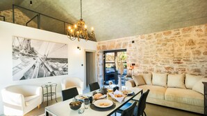 A modern living room with a dining area, stone walls, a chandelier, and a large sailboat painting.