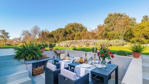 An outdoor patio with wicker furniture, a stone wall, and potted plants.