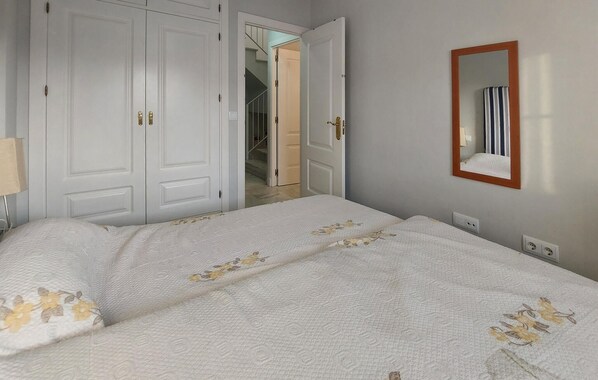 A bedroom with a bed, a wardrobe, a mirror, and a door leading to another room.