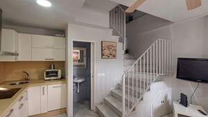 A modern kitchen with white cabinets, a built-in microwave, and a sink. There is a staircase leading to a landing with a TV and a small table. - Awesome home in Rota with WiFi (Rota)