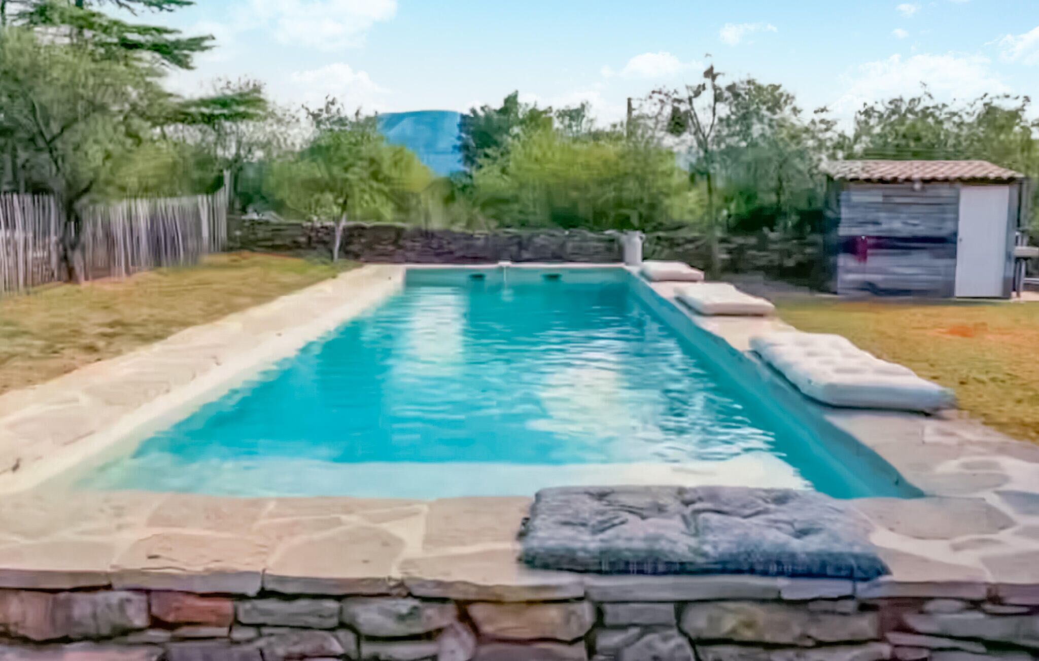 Une piscine rectangulaire bordée de pierres, avec un mur de pierres en premier plan.