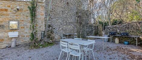 A rustic outdoor seating area with stone walls and a gravel ground, featuring a table and chairs.