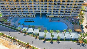 A high-rise hotel with multiple balconies, a central swimming pool, and outdoor seating areas.