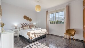 A modern bedroom with a bed, bedside tables, a chair, a window, and a decorative wall piece. - Las Cuatro Flores Órgiva by Ruralidays (Granada)