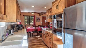 A kitchen with wooden cabinets, a stainless steel refrigerator, a double sink, and a dining area with a red tablecloth. - Inside Yosemite Park 3BR Sleeps 8 Game Loft (Yosemite Valley)
