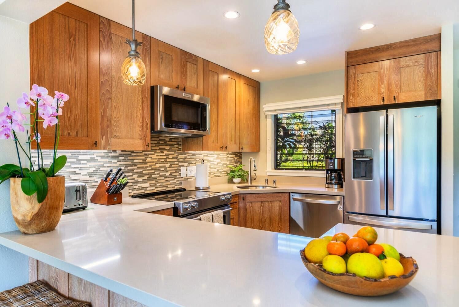 A modern kitchen with wooden cabinets, stainless steel appliances, and a large island with a fruit bowl.