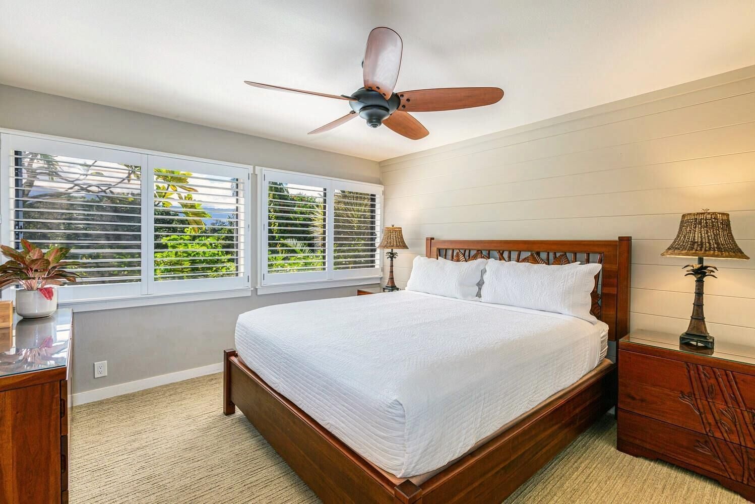 A bedroom with a wooden bed, a ceiling fan, two bedside tables with lamps, and a window with blinds.