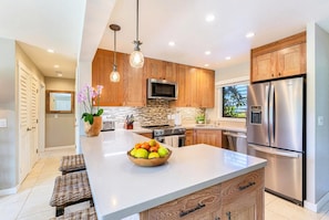 A modern kitchen with wooden cabinets, stainless steel appliances, and a central island with a fruit bowl.