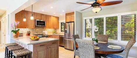 A modern kitchen with wooden cabinets, a central island, and a dining area with wicker chairs.