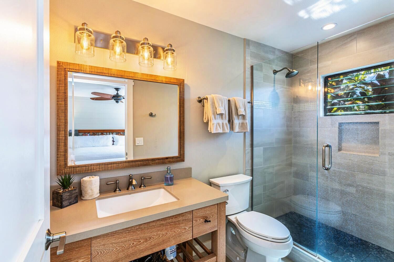 A modern bathroom with a large mirror, a wooden vanity, a toilet, and a glass shower enclosure.
