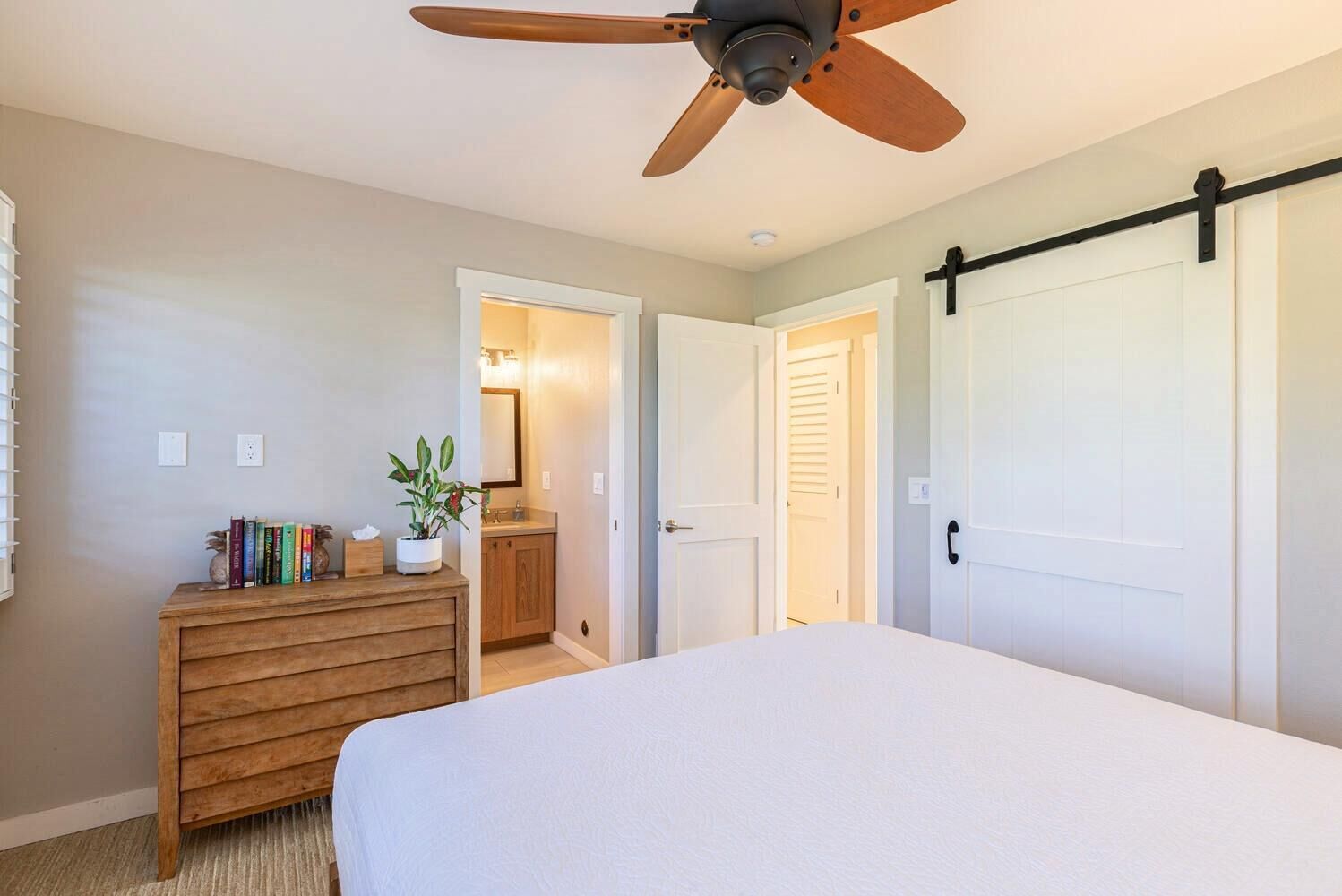 Un dormitorio con cama, cómoda de madera, ventilador de techo y puerta corredera.