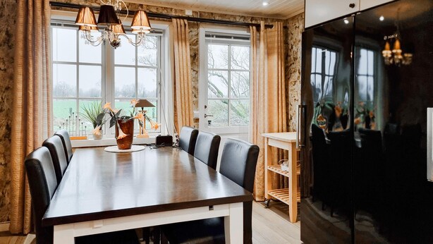 Een eetruimte met een houten tafel, zwarte stoelen, een vaas met bloemen en een zwarte koelkast.