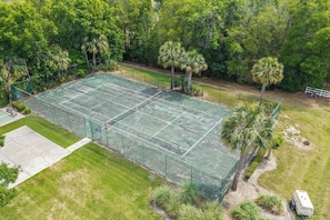 Cancha de tenis rodeada de árboles y una cerca blanca.