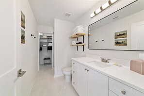 Bathroom features a white vanity, sink, and toilet, with towel racks and a shelf for added convenience.