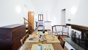 Un coin repas avec une table en bois dressée pour quatre personnes, une cuisine en arrière-plan et un escalier menant à un autre niveau.