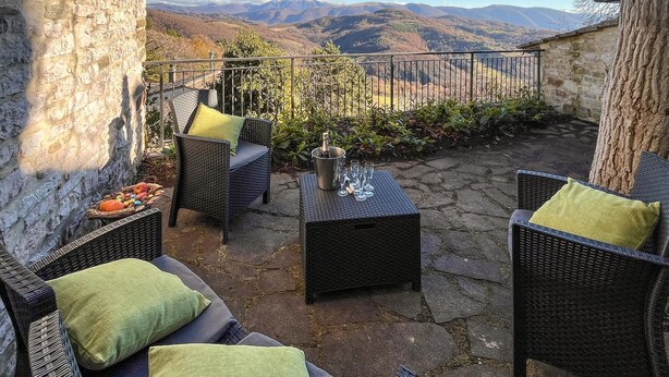 Une terrasse dotée de meubles en osier, d’une table en pierre et offrant une vue sur les montagnes.