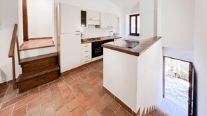 Une cuisine avec des meubles blancs, un escalier en bois et une fenêtre donnant sur un espace extérieur enneigé.