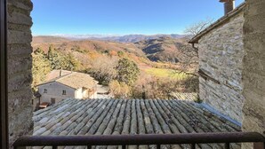 Un bâtiment en pierre, doté d’un toit en tuiles, qui surplombe une vallée avec des montagnes à l’horizon.