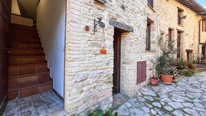 Un bâtiment en pierre avec un escalier en bois, une porte et des plantes en pot au rez-de-chaussée.