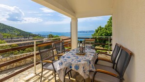 A balcony with a table and chairs, overlooking a scenic view of the sea and hills.