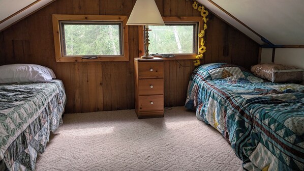 A cozy attic bedroom with two beds, a dresser, and a lamp. - Sunset Point Cabin (Marcell)