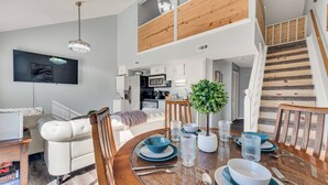 A modern living room with a dining area, a staircase, and a kitchen in the background. - Home of Light, Branson, Mo (Branson)