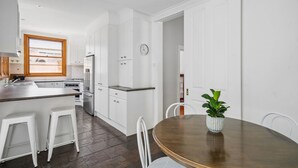 A modern kitchen with white cabinetry, a wooden countertop, and a dining area with a round table and white chairs. - Charming House in Woolwich (Woolwich)