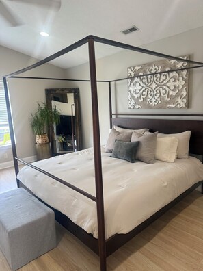 Un lit à baldaquin avec une tête de lit, un pouf gris et un élément décoratif mural.