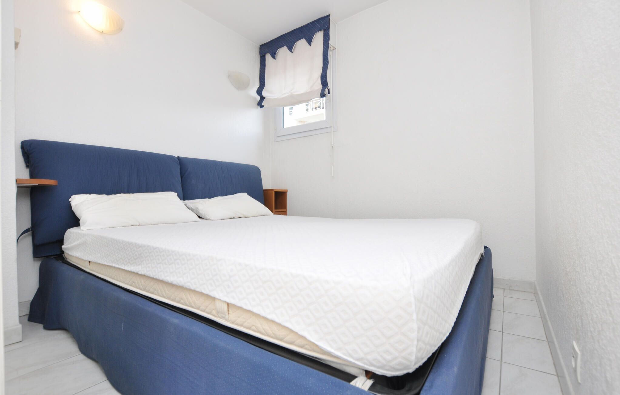 Habitación individual con una cama que tiene un cabecero azul, ropa de cama blanca y una mesita de noche de madera.