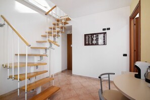 Un escalier avec des marches en bois et des rampes blanches, une œuvre d’art accrochée au mur, une table avec une bouilloire et une chaise.