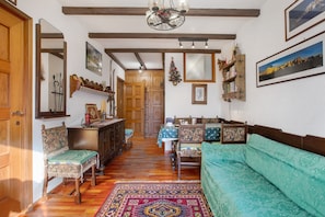 Una habitación tradicional con suelos de madera, un sofá verde, una mesa de comedor de madera y un espejo.