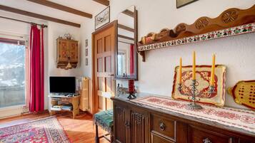 Habitació amb un armari de fusta, televisió, cortina vermella, alfàbregua estampada i una estantanya penjada a la paret amb un objecte decoratiu.