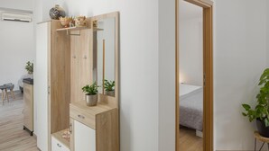 A modern bedroom with a wooden wardrobe, a bedside table with a plant, and a bed with a white duvet.