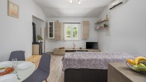 A compact, modern room with a dining table, chairs, a bed, a TV, and a kitchenette.