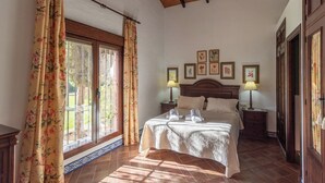 Ein Schlafzimmer mit einem Bett, zwei Nachttischen mit Lampen, einem Fenster mit Vorhängen und einer Wand mit gerahmten Bildern.