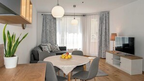Ein modernes Wohnzimmer mit einem runden Esstisch, einem grauen Sofa und einem Fernseher auf einem weißen Schrank.