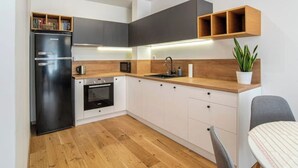 Eine kompakte Küche mit schwarzem Kühlschrank, einer Mikrowelle, einem Einbauofen, Holz Arbeitsplatten und weißen Schränken.