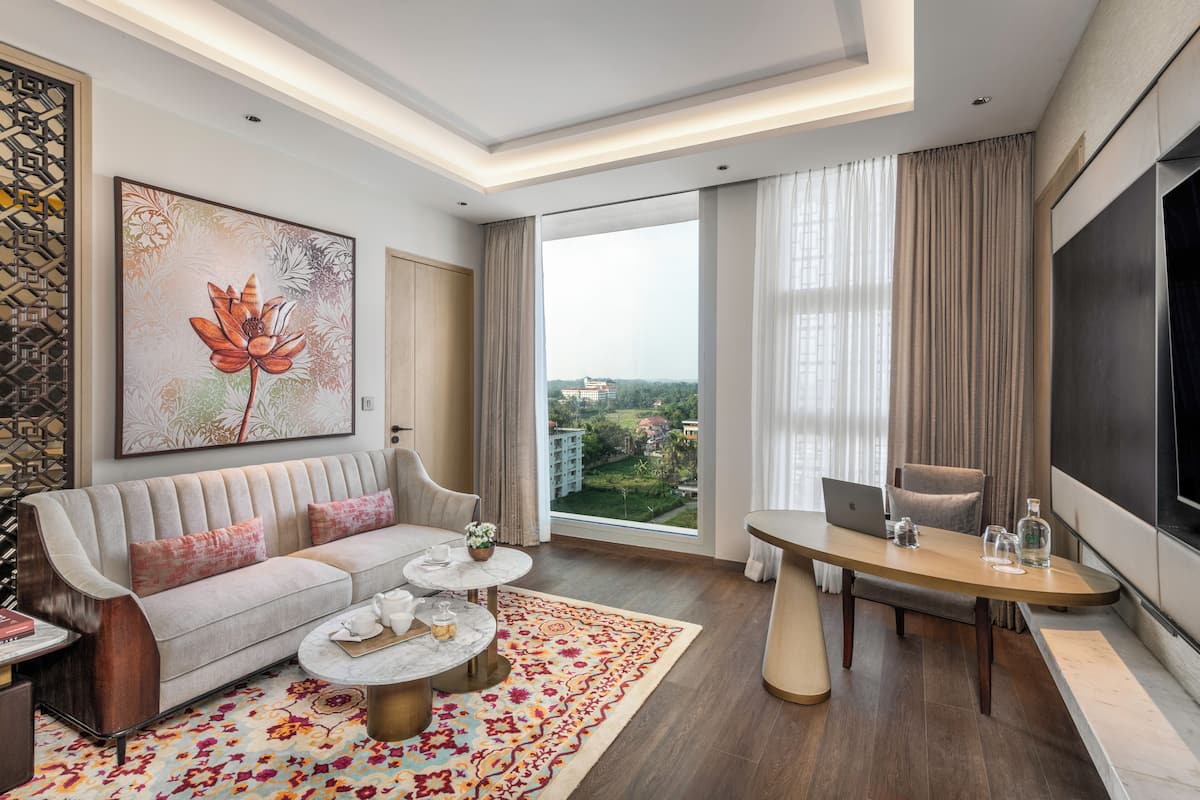 Une chambre d’hôtel moderne dotée d’un canapé, d’une table basse et d’une table à manger, de grandes fenêtres offrant une vue sur la ville et d’un téléviseur à écran plat.
