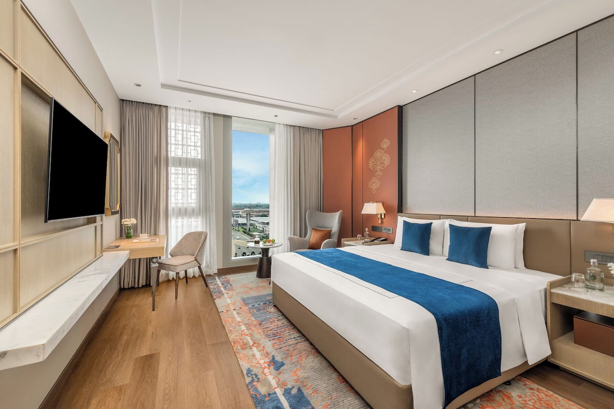 Une chambre d’hôtel moderne dotée d’un grand lit, d’un bureau, d’une chaise, d’une télévision et offrant une vue sur la ville.
