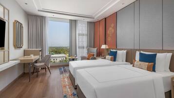Ein Hotelzimmer mit zwei Betten, einem Schreibtisch, einem Stuhl, einem Fernseher und Blick auf die Stadt.