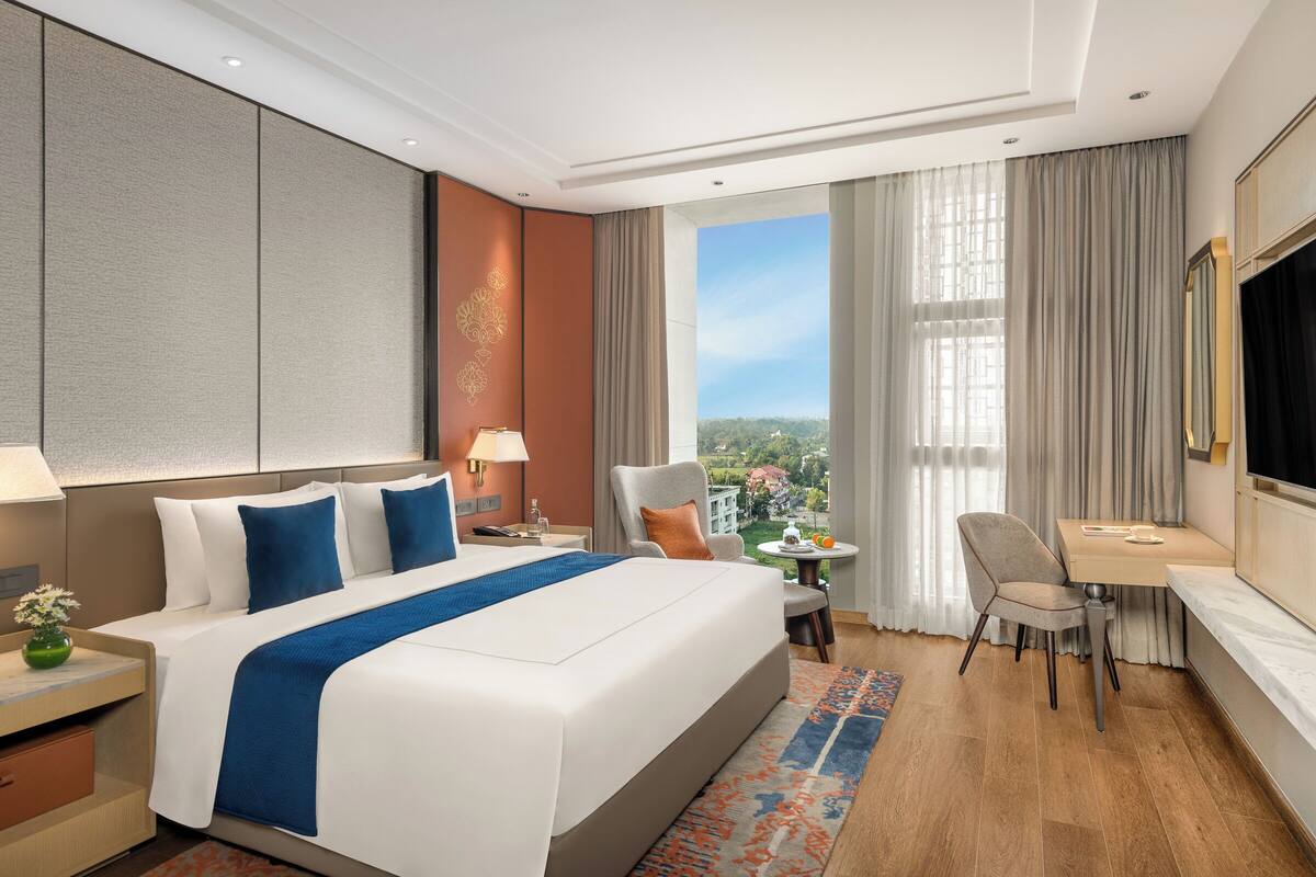 Une chambre d’hôtel avec un grand lit, un bureau et une chaise. Il y a une fenêtre donnant sur un paysage verdoyant.