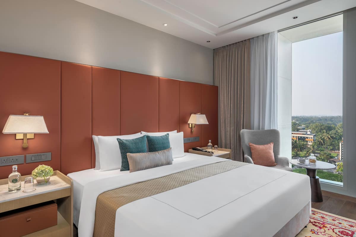 Une chambre d’hôtel avec un grand lit, deux tables de chevet, une chaise, une petite table et une vue sur la ville.
