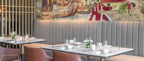 A restaurant with a mural depicting a traditional scene, cushioned seating, and a modern dining setup.