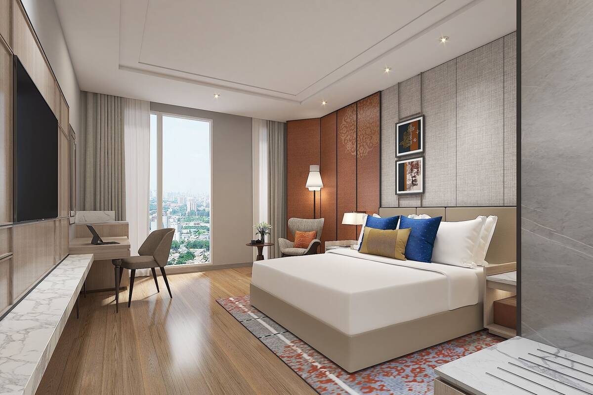 Une chambre d’hôtel moderne dotée d’un grand lit, d’un bureau avec un ordinateur portable, d’une chaise, d’une table de chevet avec une lampe et offrant une vue sur la ville grâce à de grandes fenêtres.