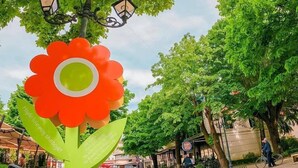 Ett offentligt torg med en stor skulptur formad som en blomma, gatlyktor och träd.