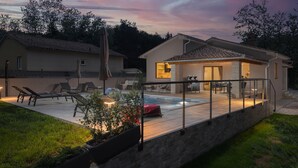 Patio esterno moderno con poltrone relax, piscina e zona salotto coperta.