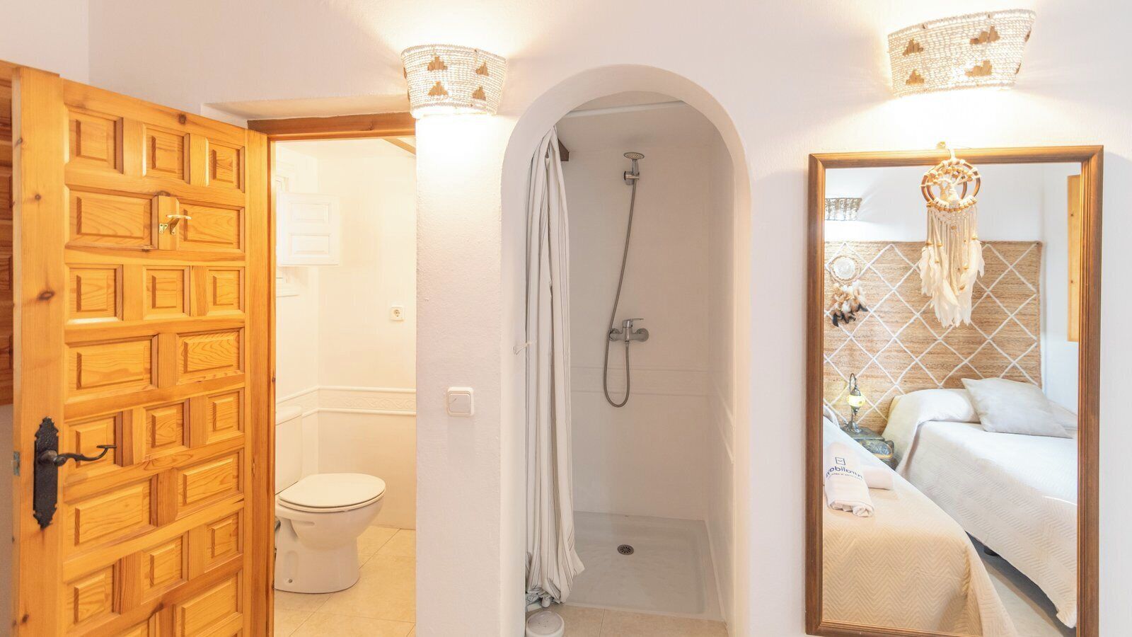 Une salle de bain avec douche, toilettes et un lit avec un miroir.